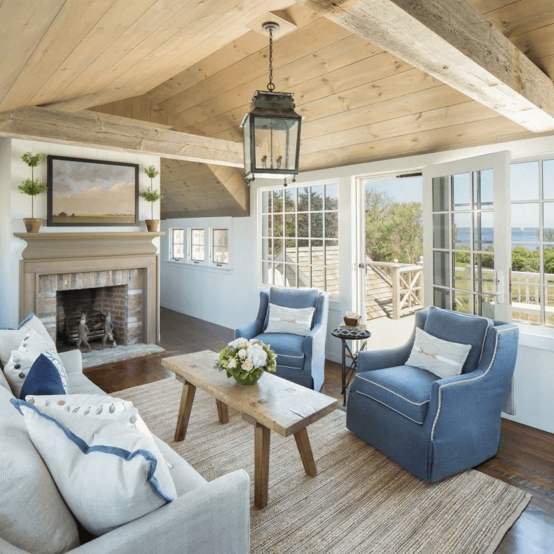 Wohnzimmer im Landhausstil mit Kamin, Holzdecke, blauen Sesseln, Holztisch und Sprossenfenstern