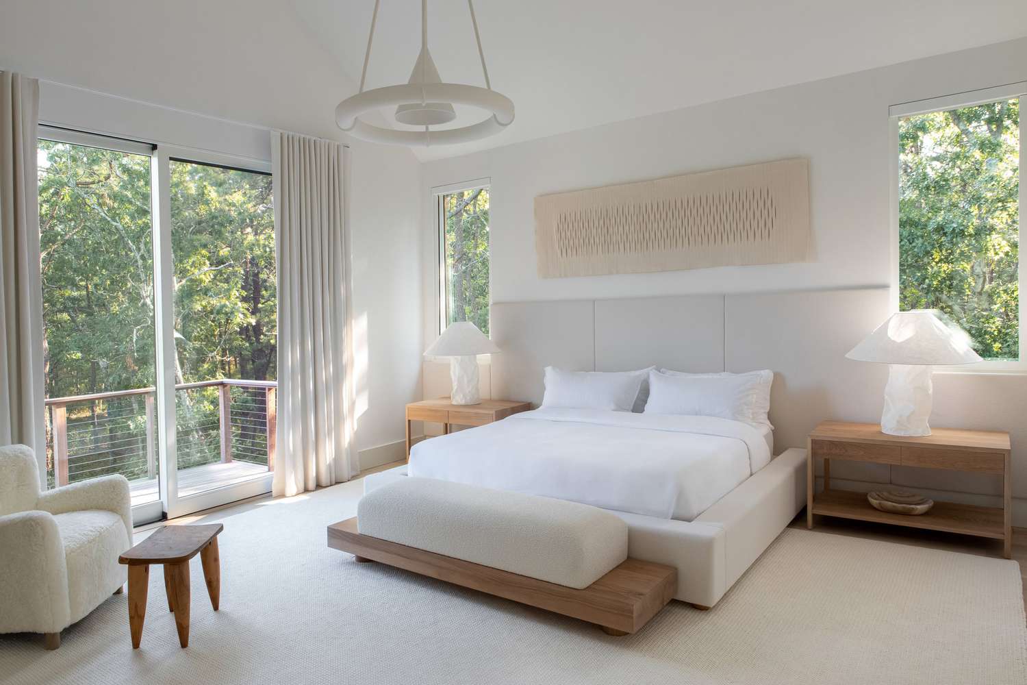 Schlafzimmer mit niedrigem Bett, Holzbank, Sessel und großer Fensterfront zum Garten